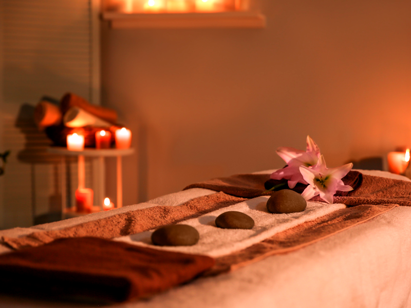 A serene spa scene with a massage table, stones, lilies, and candlelight.