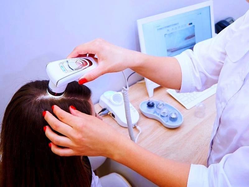 Salon professional examining a client's scalp with a digital microscope to diagnose hair loss and dandruff issues for treatment.
