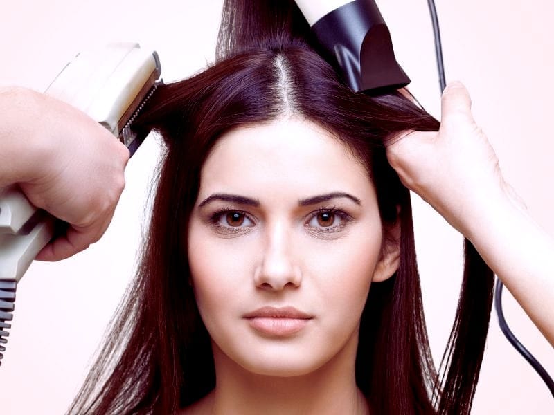 Close-up of a woman’s hair being styled, revealing dandruff on her scalp.