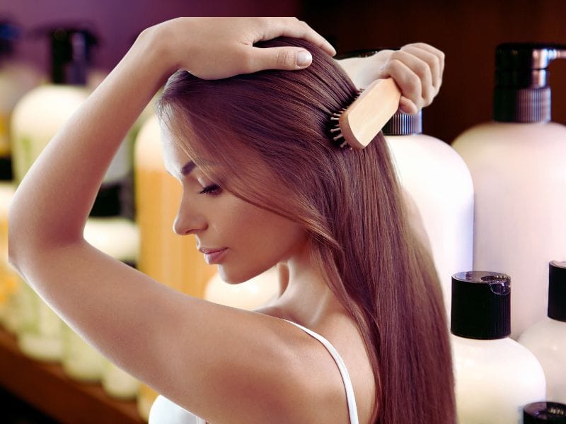 Woman brushes hair at home using salon-quality products for healthy scalp and hair care.