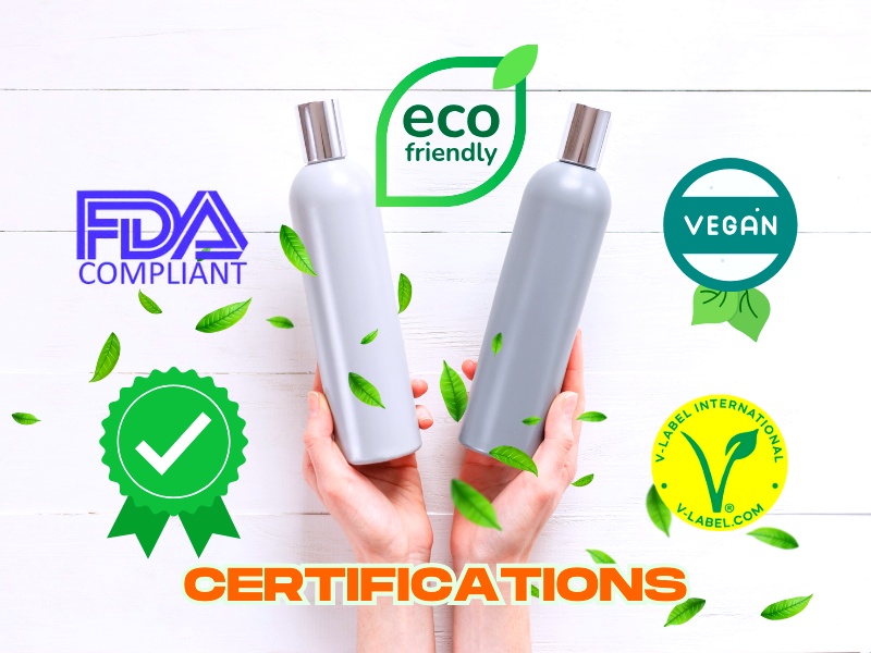 Two hands hold silver shampoo bottles with green leaves and labels for vegan, FDA compliant, eco-friendly, and V-Label International certifications.