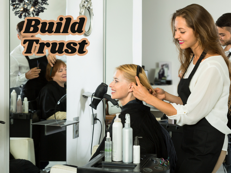 Hair stylist smiling while gently combing a client’s hair in a bright salon, with text overlay 'Build Trust' symbolizing client satisfaction and professional care.