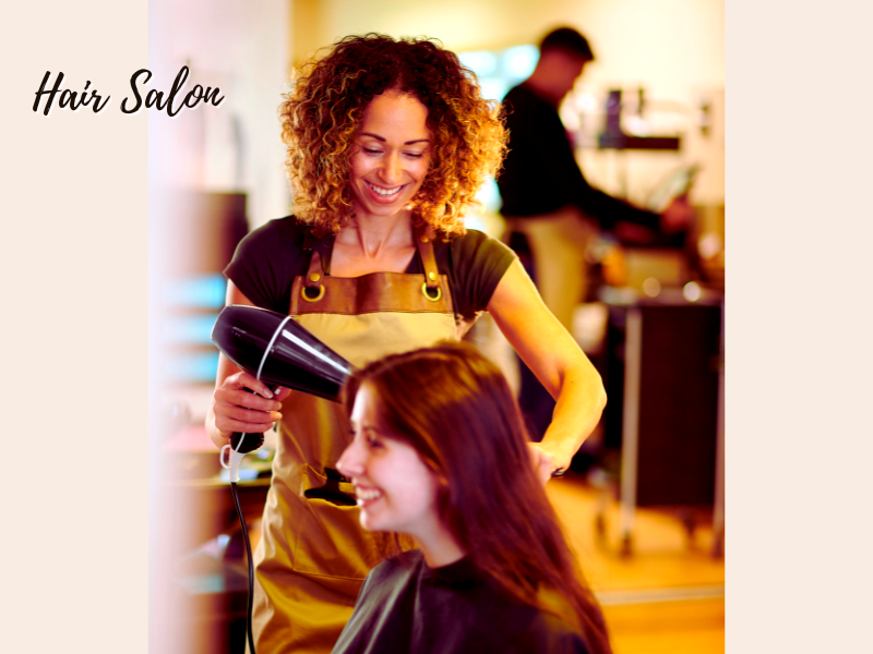 Smiling hairdresser blow-drying a client's hair in a salon, promoting the idea that salons should offer vegan haircare options.