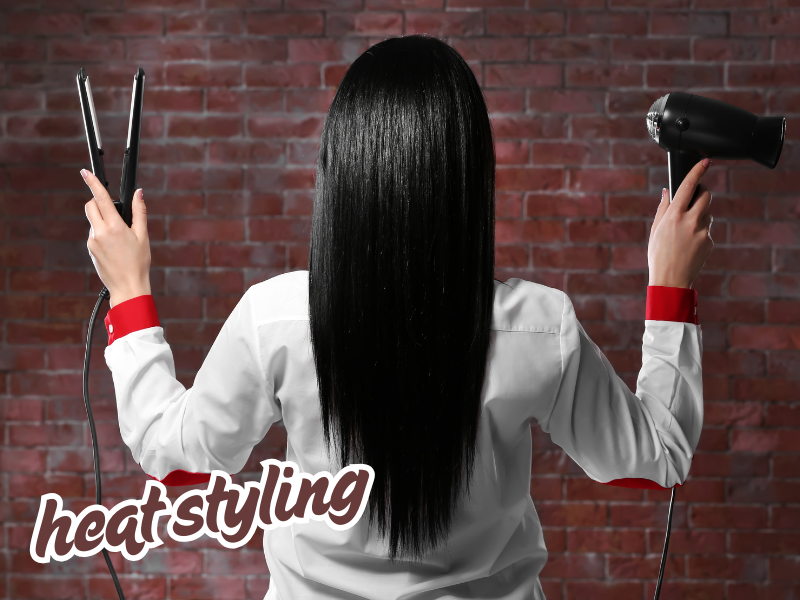 Back view of woman holding a flat iron and hairdryer, demonstrating heat styling risks for hair damage.