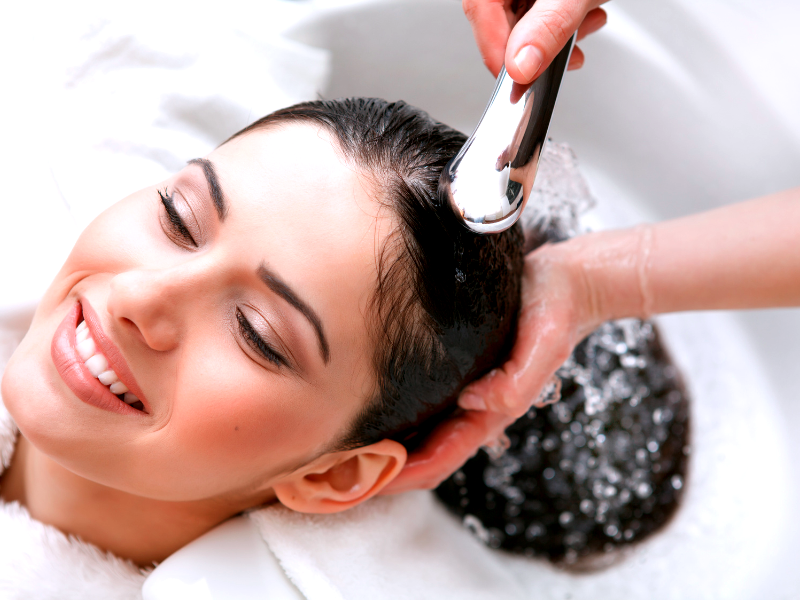 Woman smiles while getting a relaxing scalp rinse—salon scalp detox brings visible relief and joy.