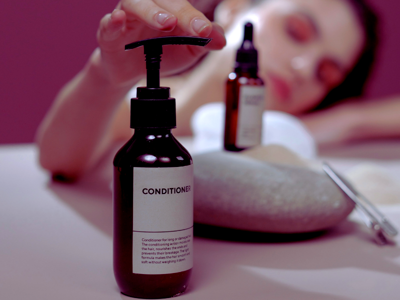 Close-up of a woman reaching for a conditioner bottle labeled sulfate-free, free of harsh ingredients.
