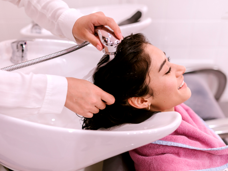 Smiling woman receiving a gentle scalp rinse at salon—highlighting chemical-free care and comfort.