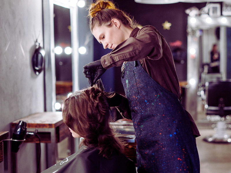 Hairdresser applying product to client’s hair at salon, promoting professional hair care routine.