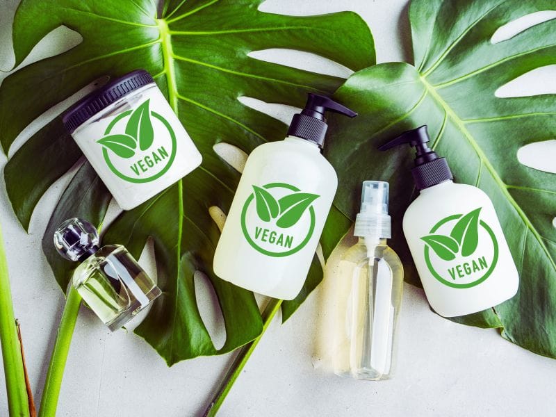 Vegan haircare bottles and jars arranged on tropical leaves, promoting natural beauty.