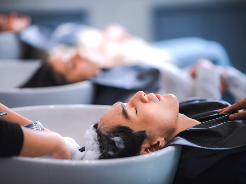 Clients getting a relaxing hair wash with foam shampoo at a salon wash station, clean beauty concept.