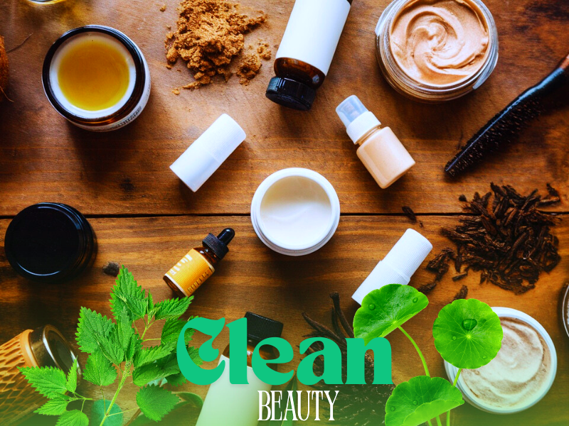 Flat lay of vegan clean beauty products with herbs, oils, and jars on wooden table.