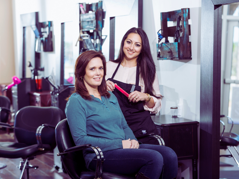 Stylist with flat iron and smiling client in salon—trust built around results-driven haircare line.