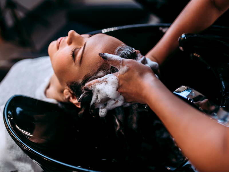 Woman enjoys relaxing shampoo at salon sink—foamy lather shows the care of a professional haircare line.