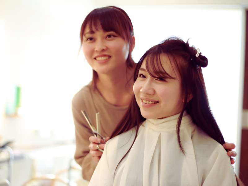 Hair stylist and client smile together during a haircut—celebrating beauty, trust, and happy service.