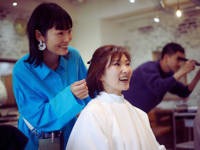 Smiling client enjoys haircut from cheerful stylist—building trust and joy in a welcoming salon space.