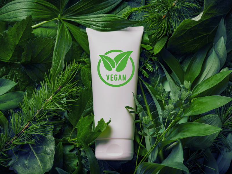 Vegan skincare or haircare product tube placed on a bed of fresh green herbs and natural leaves.