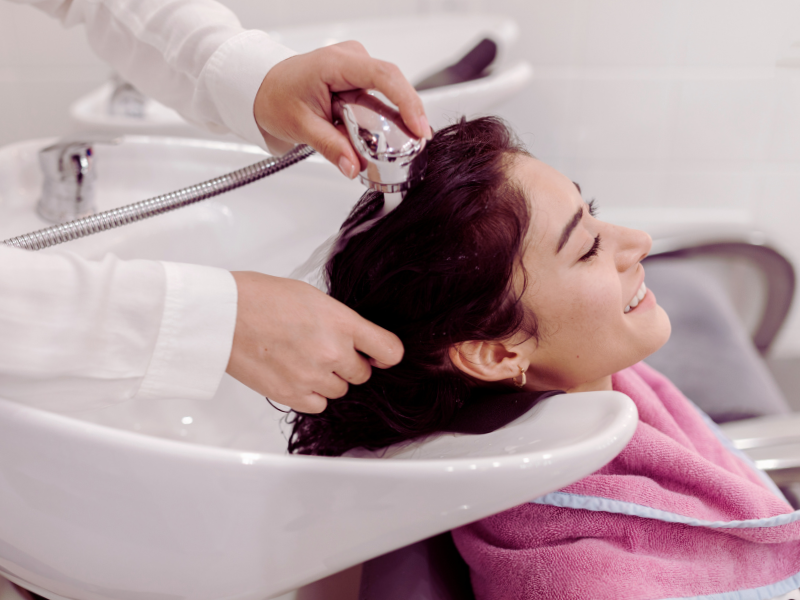 Smiling woman getting a scalp rinse at salon – relaxing hair wash with clean, scalp-friendly treatment