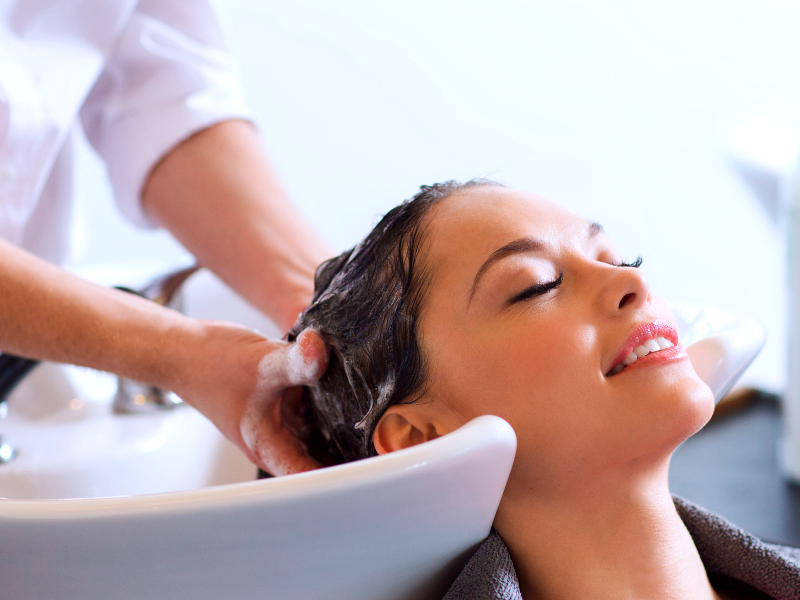Woman relaxing with eyes closed during a salon hair wash, receiving a gentle shampoo treatment at a modern basin.