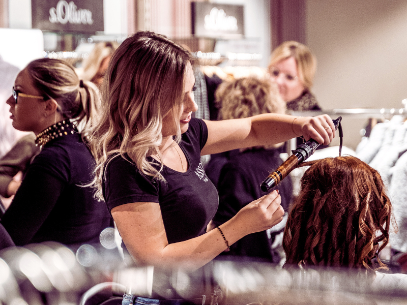 Salon professional styling hair with heat tools during a busy appointment, highlighting skilled services and client care.