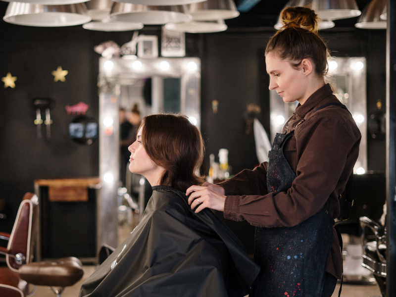 Hairdresser giving a relaxing scalp massage to a seated woman client inside a stylish modern salon.